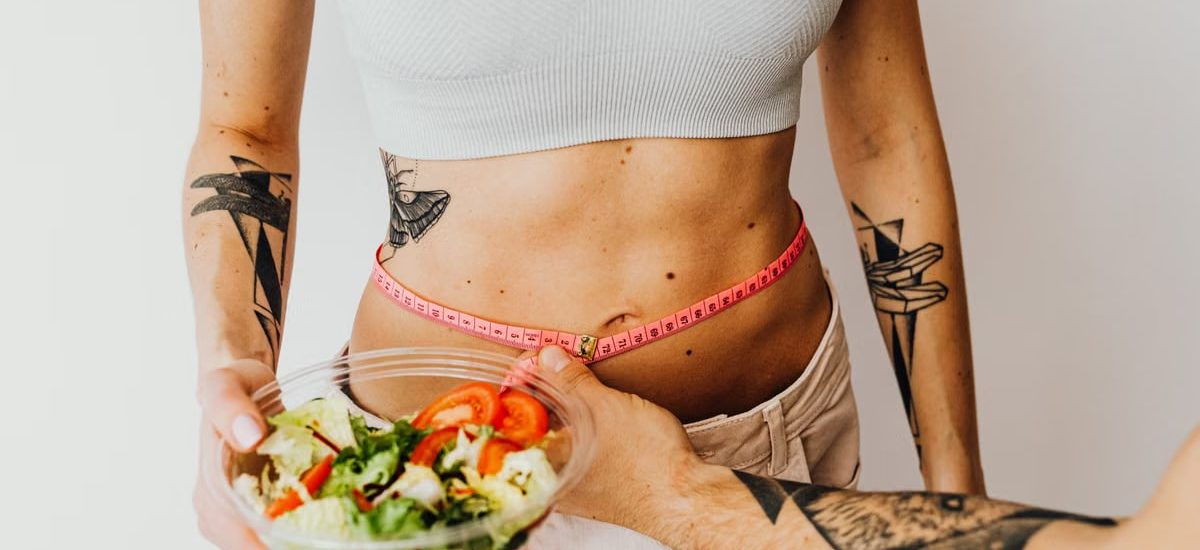 Fit woman measuring waist while holding a healthy salad bowl