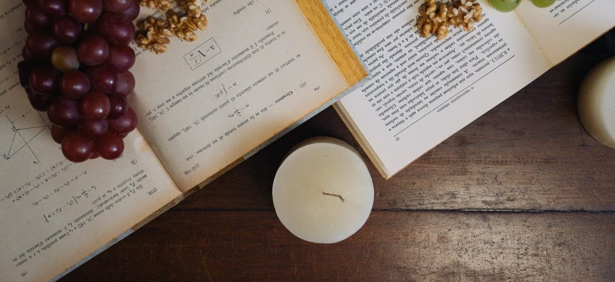 Aesthetic still life with grapes, walnuts, and open books by candlelight on a wooden table.