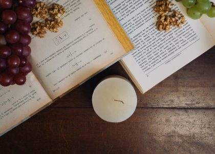 Aesthetic still life with grapes, walnuts, and open books by candlelight on a wooden table.